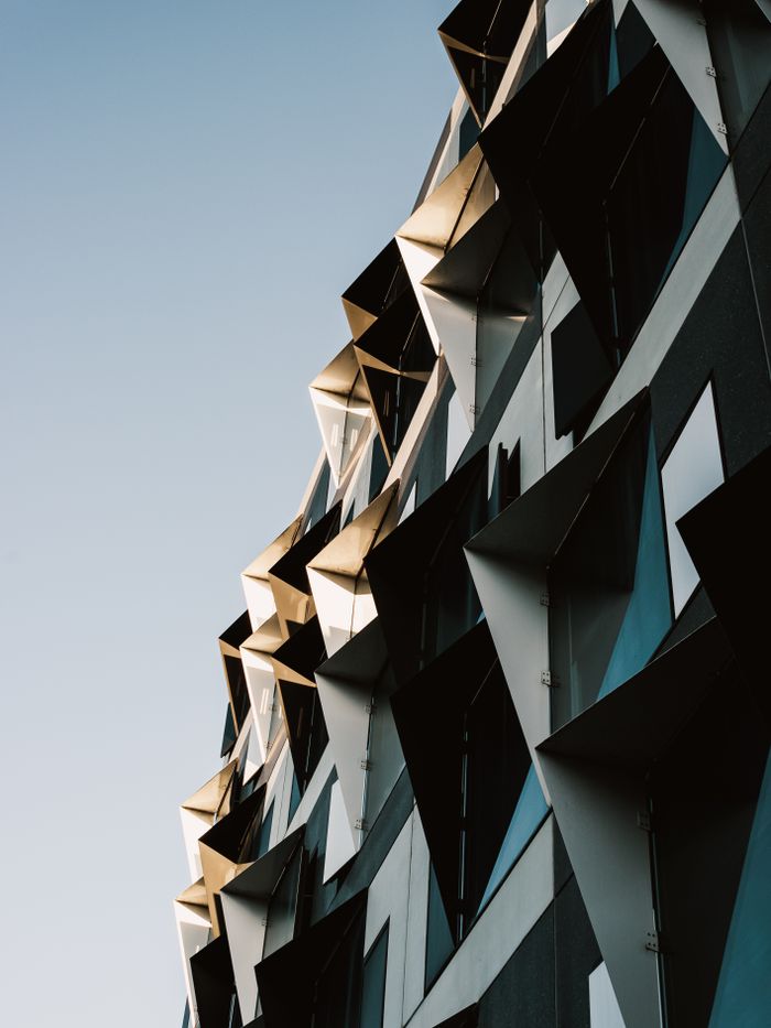 get-in-touch A close-up view of a modern building facade with geometric patterns and sharp angles.